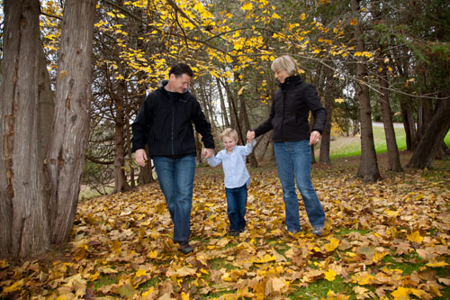 Family Portrait - Mom and Dad holding Childs Hands walking through the Fall Leaves